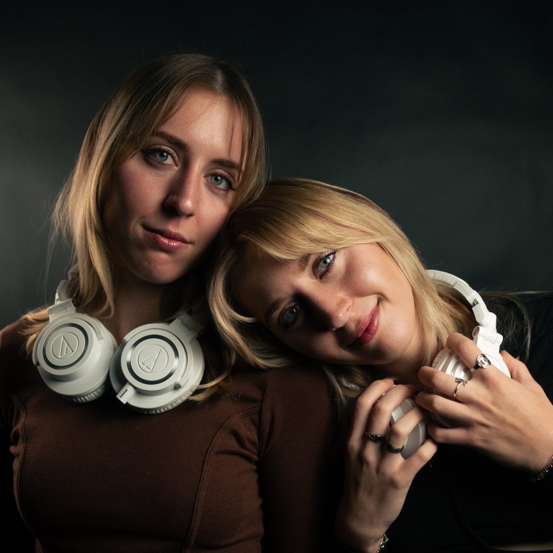 The TWINEM twins with white headphones on a dark studio backdrop